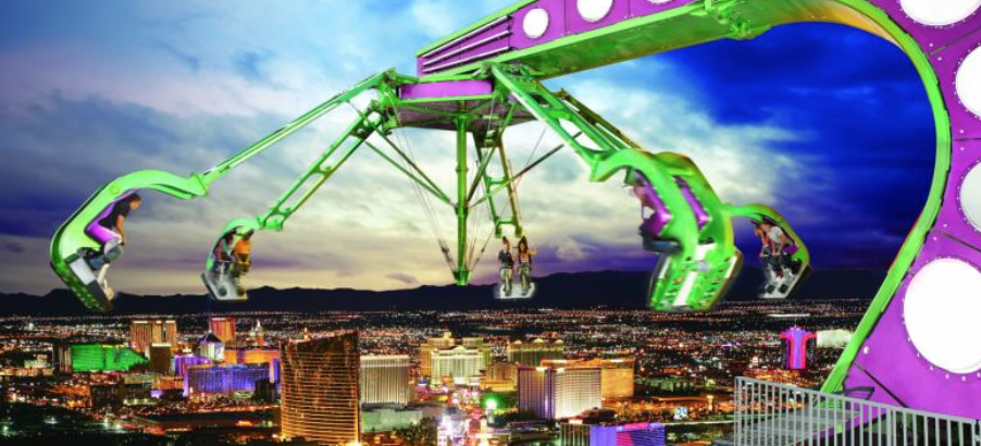 A photo of the ride Insanity in full motion. It is dangling over the side of the Strat with a view of the Vegas skyline in the background.