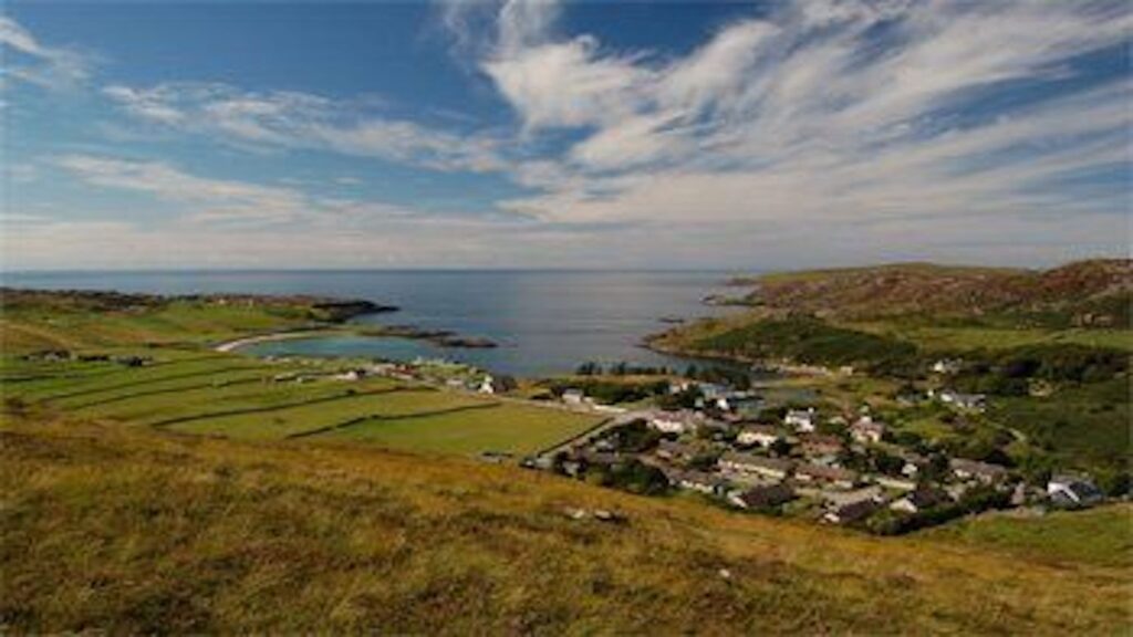 Small town of Scourie pictured from above with view of coastline and houses.