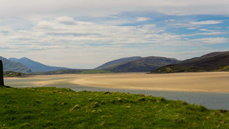 This image is looking out over the Kyle of Durness. You can see the large spanning sand banks and blue water. In the distance there are mountains and blue skies.